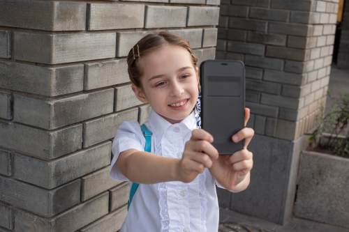 摄图网_506276353_微笑美丽的青春期前女孩在户外自拍孩子用手机自拍技术和通信概念女学生在街上自（企业商用）